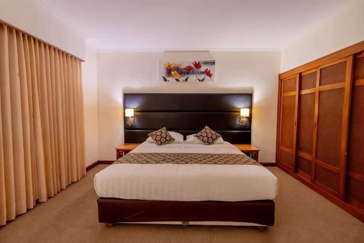 Une chambre d’hôtel avec un grand lit, une tête de lit, une table de chevet, une œuvre d’art accrochée au mur et une armoire en bois.