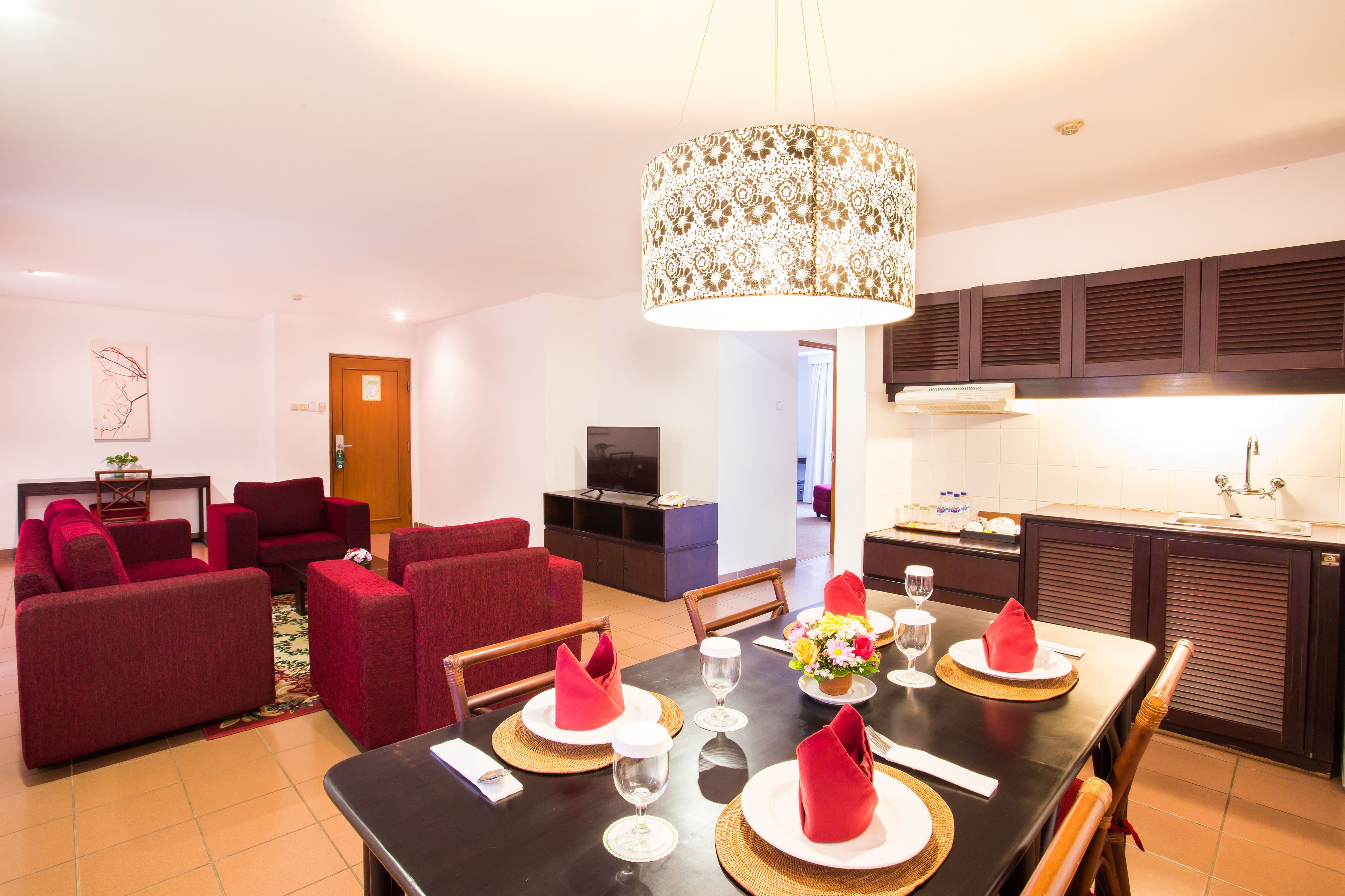 A hotel room with a dining area, red sofas, a black dining table set for four, and a kitchen in the background.