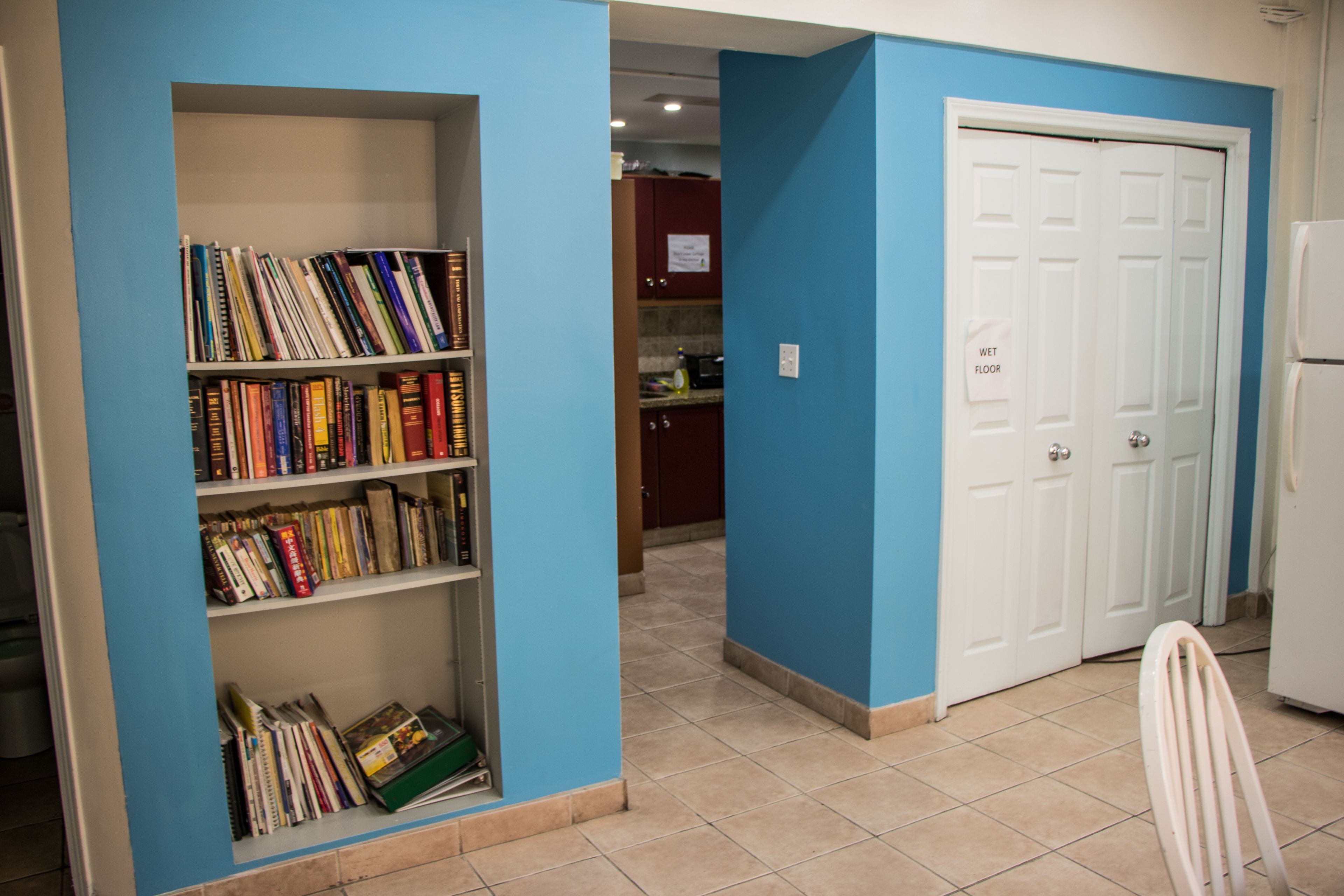 A room with a bookshelf, a white door, and a kitchen area.