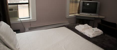 A hotel room with a bed, a television, and a window with blinds.
