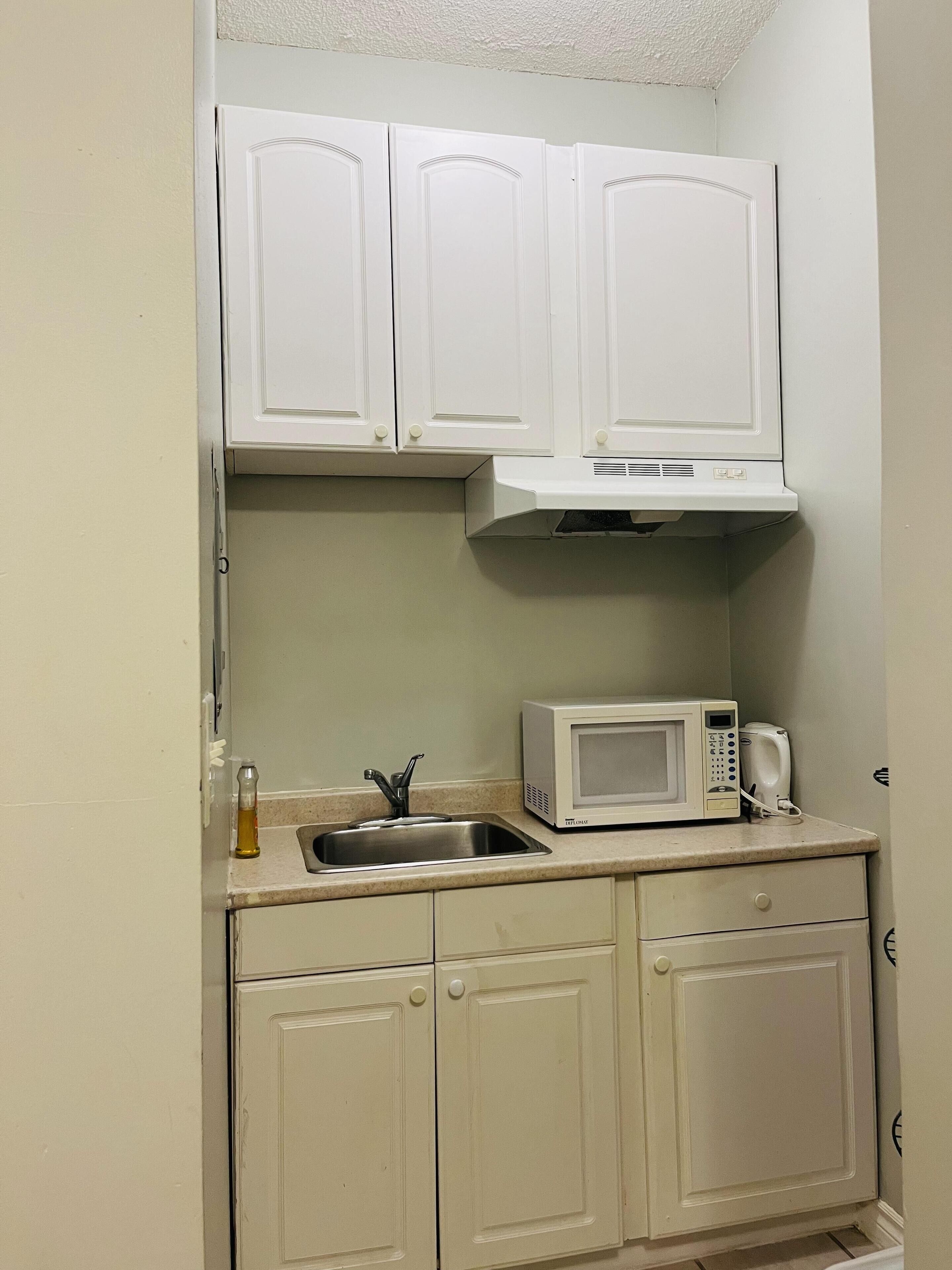 A compact kitchenette with white cabinets, a microwave, a toaster, and a sink.