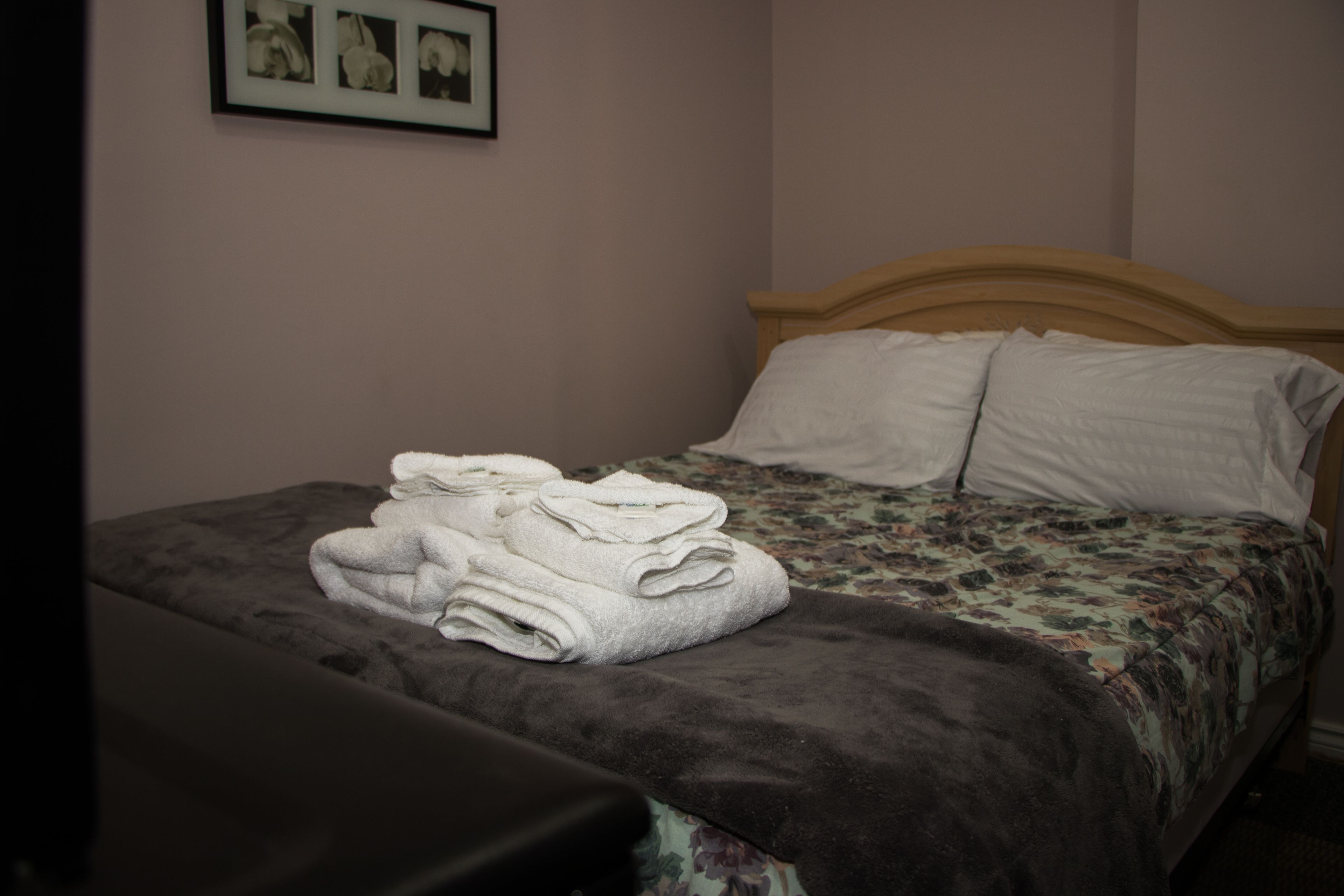 A neatly made bed with a floral bedspread and two pillows, a folded towel on the bed, and a framed picture on the wall.