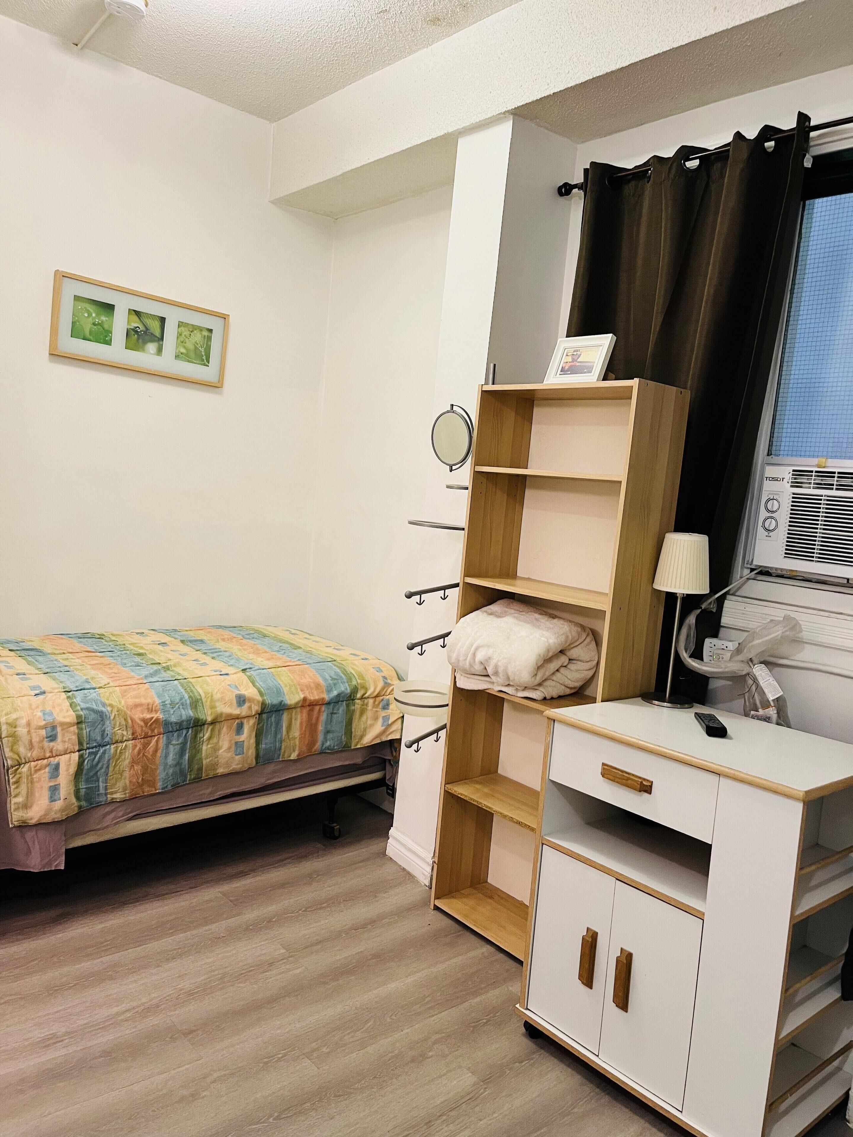 Une chambre à coucher avec un lit, une table de chevet avec une lampe, une armoire et une fenêtre avec des rideaux.