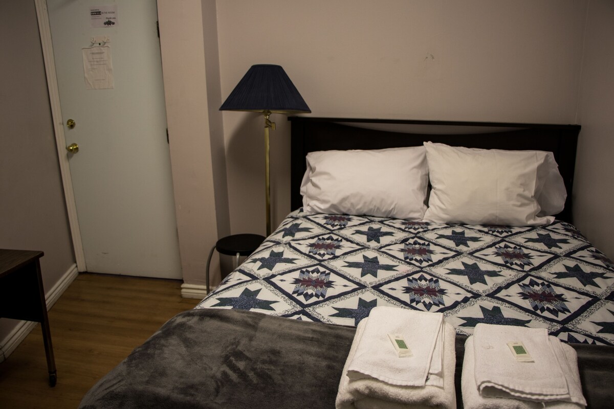 A hotel room with a bed, a nightstand, a lamp, and a door with a notice.