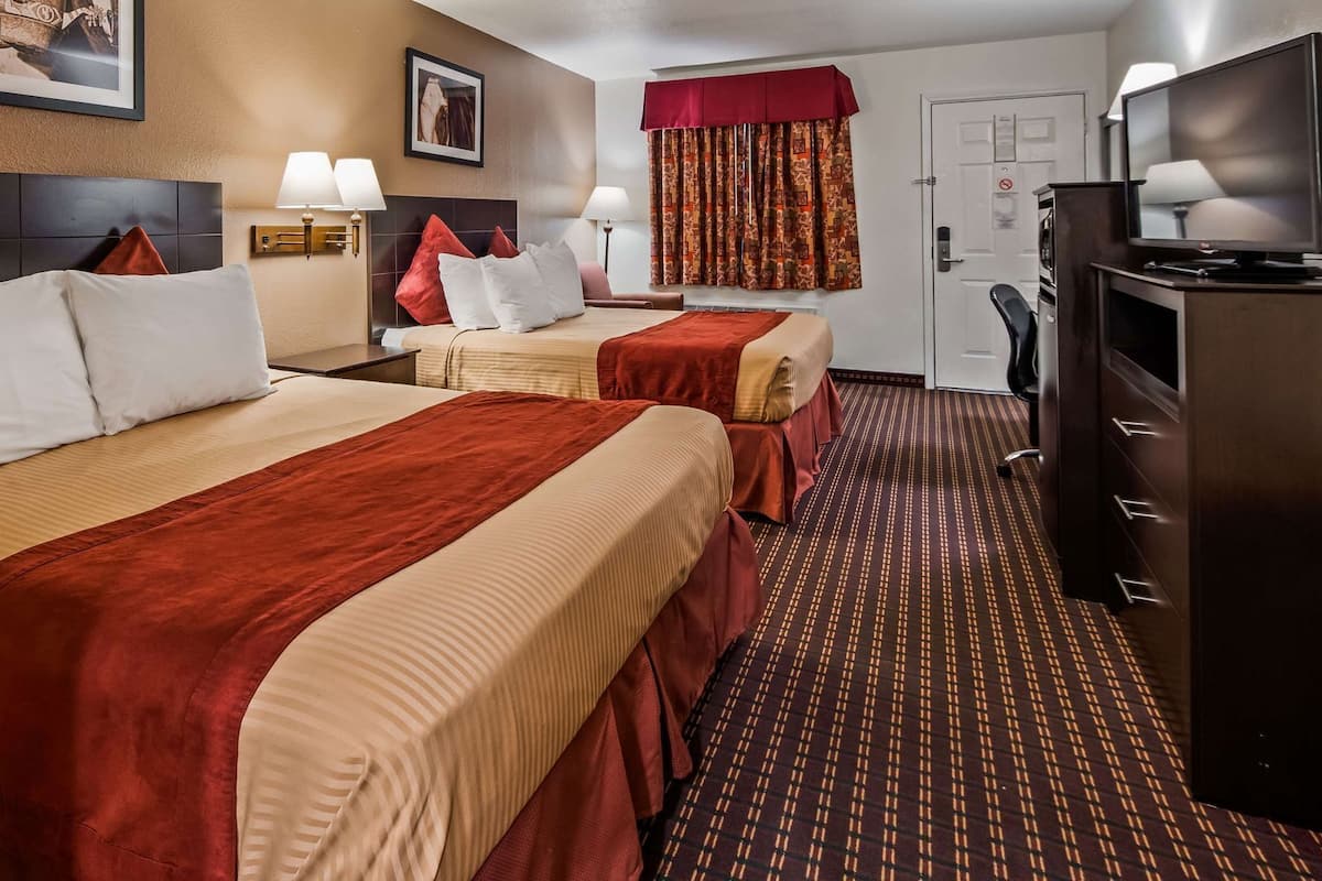 A hotel room with two beds, a television, a desk, and a bathroom.