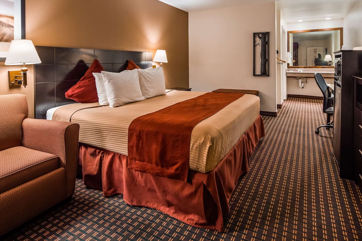 A hotel room with a bed, a desk, a chair, a television, and a bathroom with a mirror and sink.