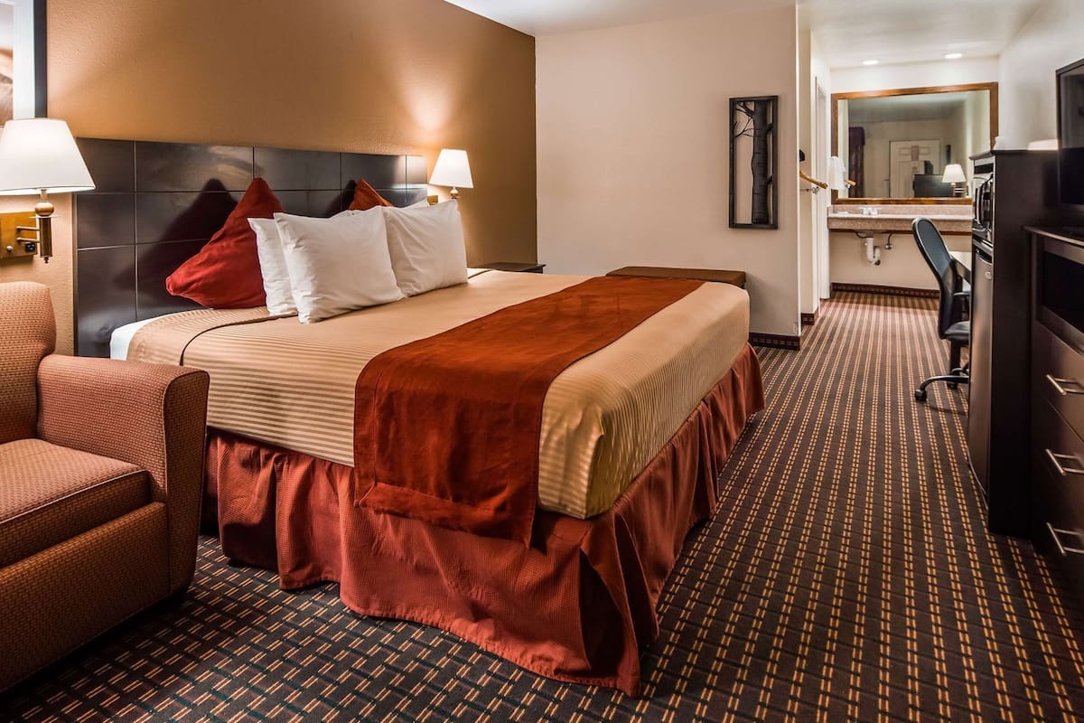 A hotel room with a bed, a desk, a chair, a television, and a bathroom visible in the background.