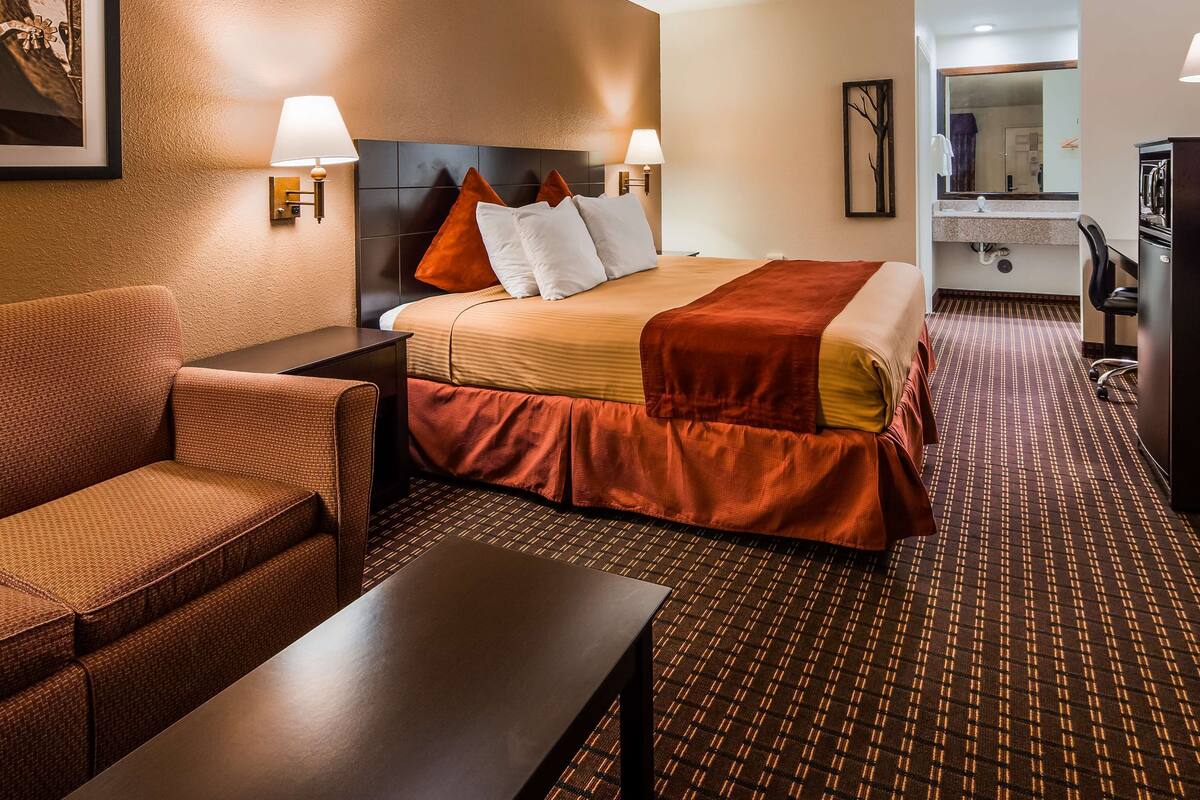 A hotel room with a bed, a sofa, a desk, and a bathroom visible in the background.