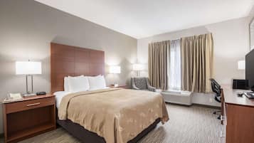 A hotel room with a bed, bedside lamps, a desk with a computer, a chair, and a window with curtains.