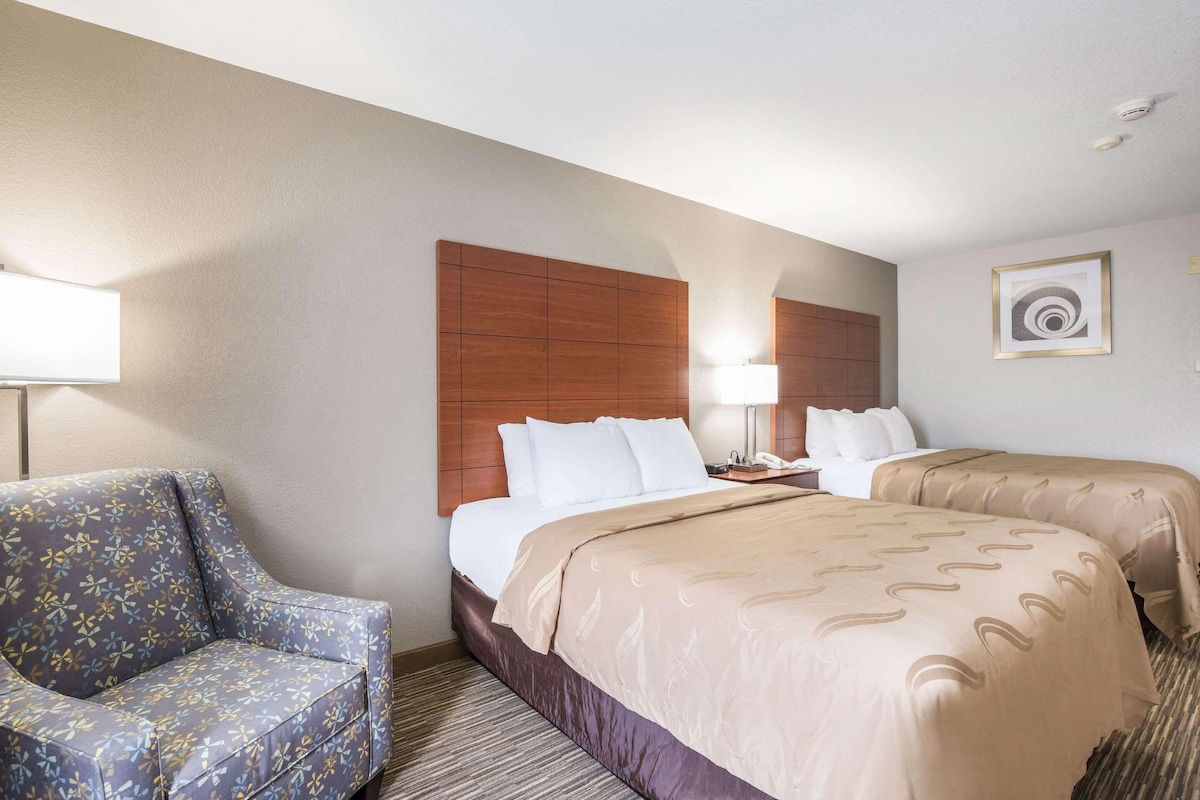 A hotel room with a large bed, two bedside tables, a chair, and a wall-mounted artwork.