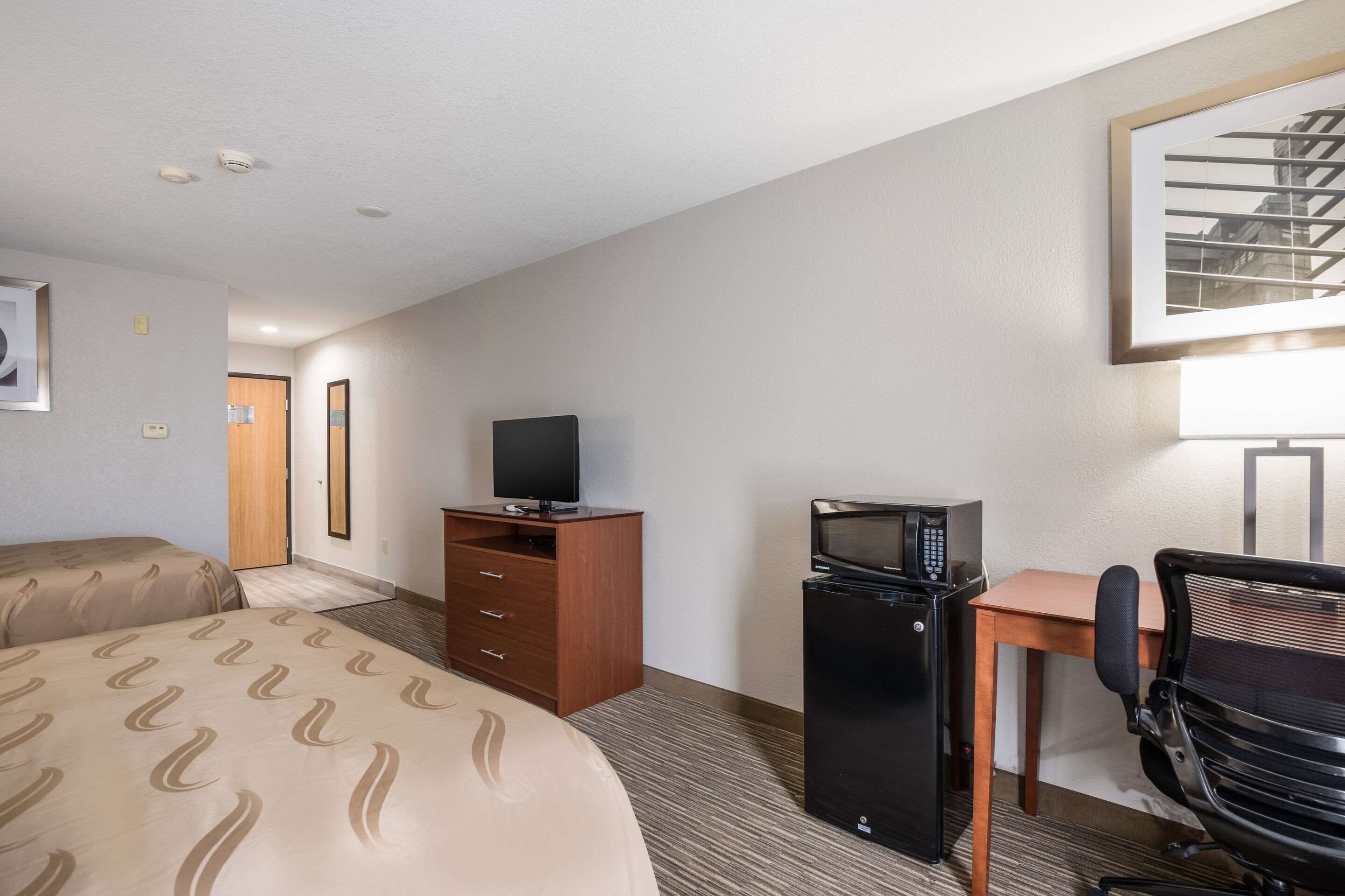 A hotel room with a bed, a desk with a computer, a television, and a microwave.