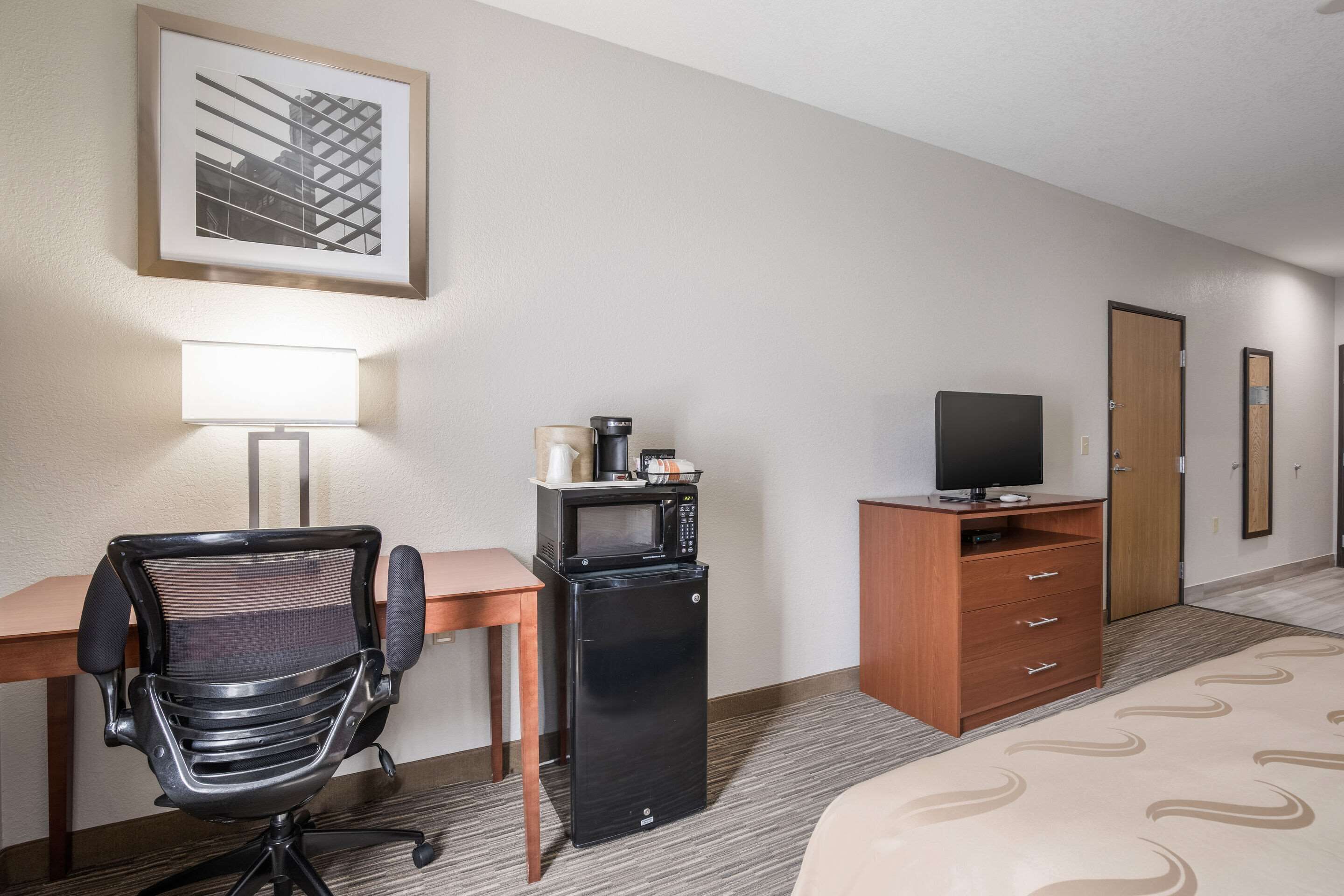 Een hotelkamer met een bureau, een stoel, een magnetron, een televisie, een kast en een bed.