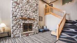 Una chimenea de piedra con repisa, una escalera de madera y una alfombra estampada.