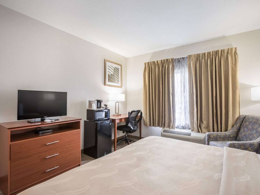 A hotel room with a bed, a desk with a computer, a television, and a chair.
