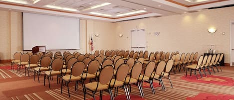 A conference room with rows of chairs, a podium, a projector screen, and an exit sign.