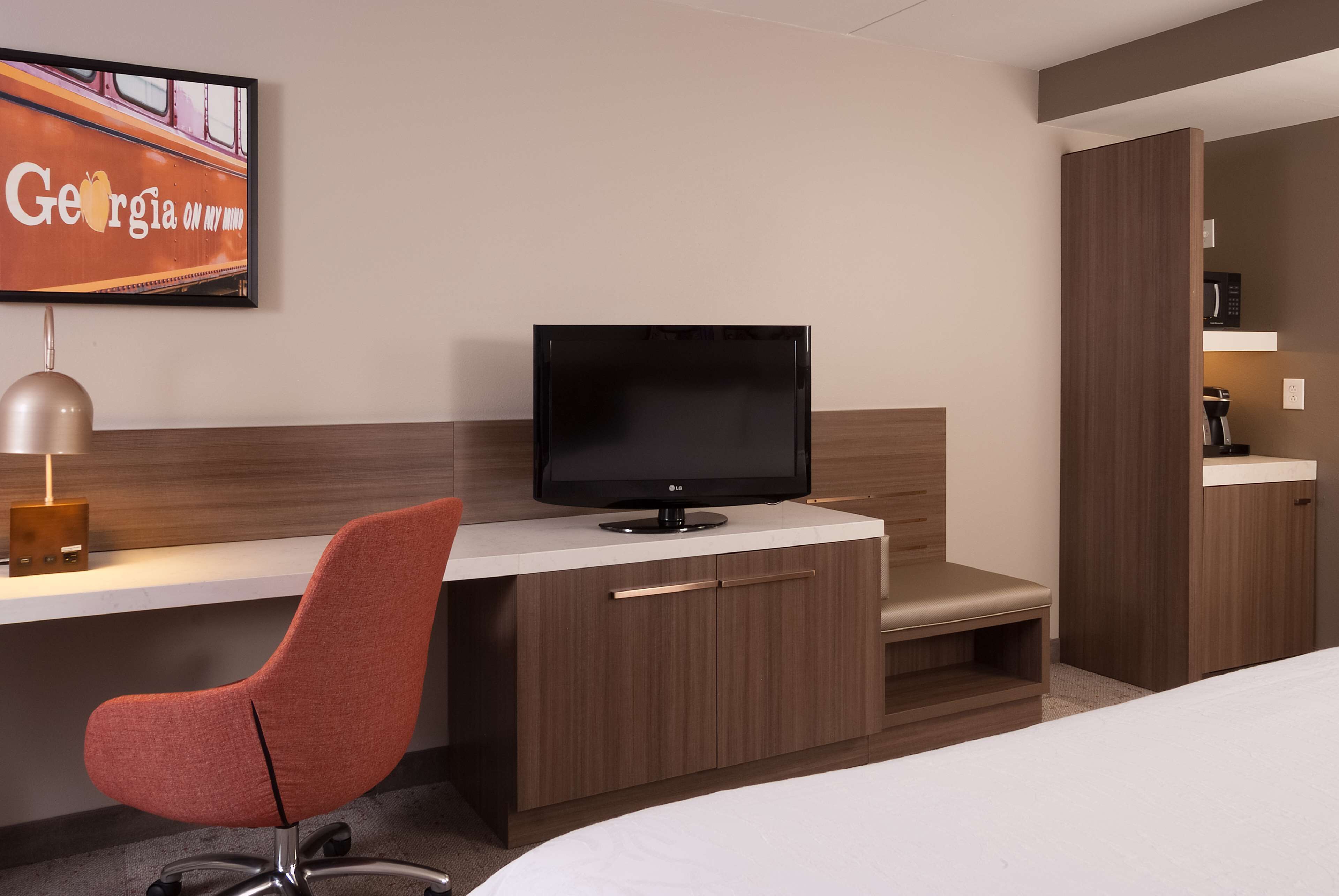 Habitación de hotel con escritorio, televisión, silla, cama y armario.
