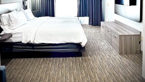 A modern hotel room with a large bed, a flat-screen TV, a wooden dresser, and a large window with curtains. - Holiday Inn Express Hinesville by IHG (Hinesville)