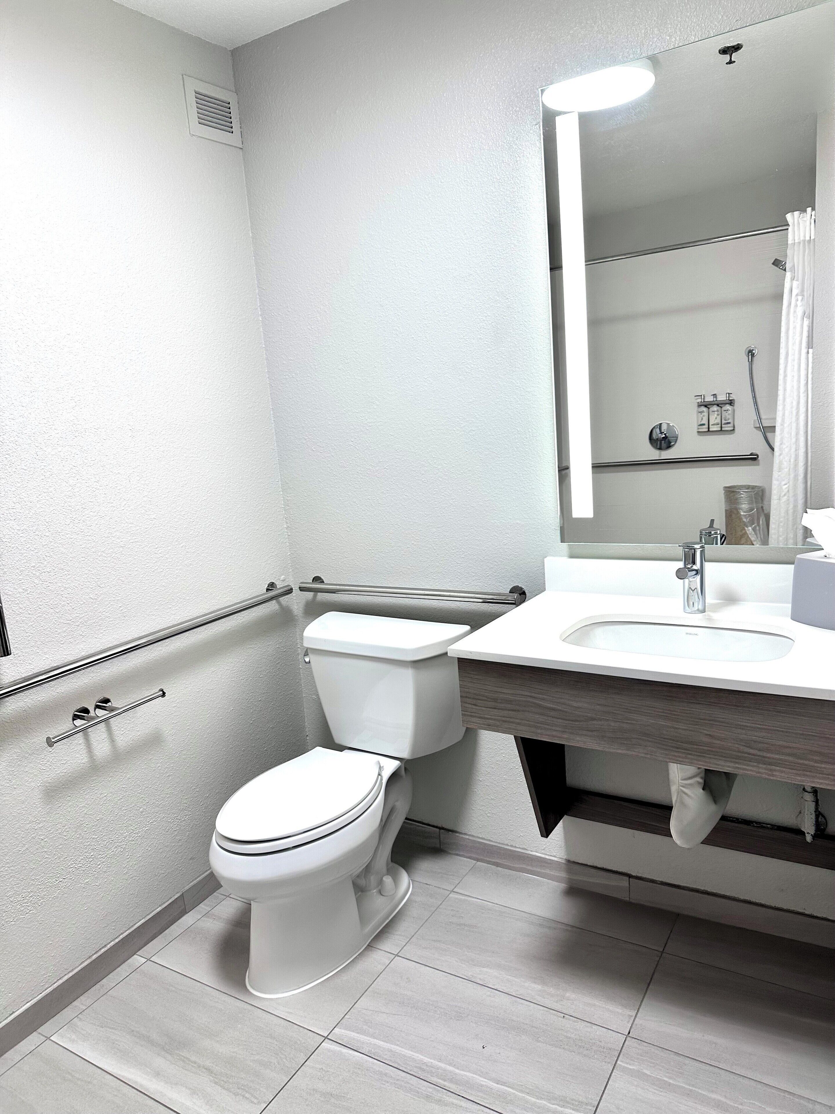 Et moderne badeværelse med toilet, håndvask med spejl og bruseområde.