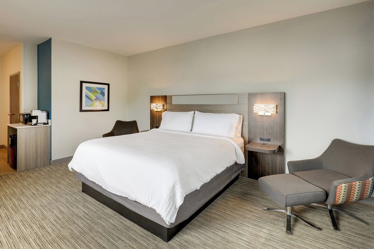 A modern hotel room with a large bed, a desk with a chair, and a sofa.