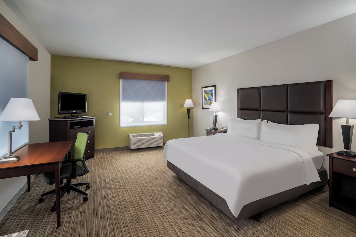 A hotel room with a bed, desk, chair, television, and a window with blinds.