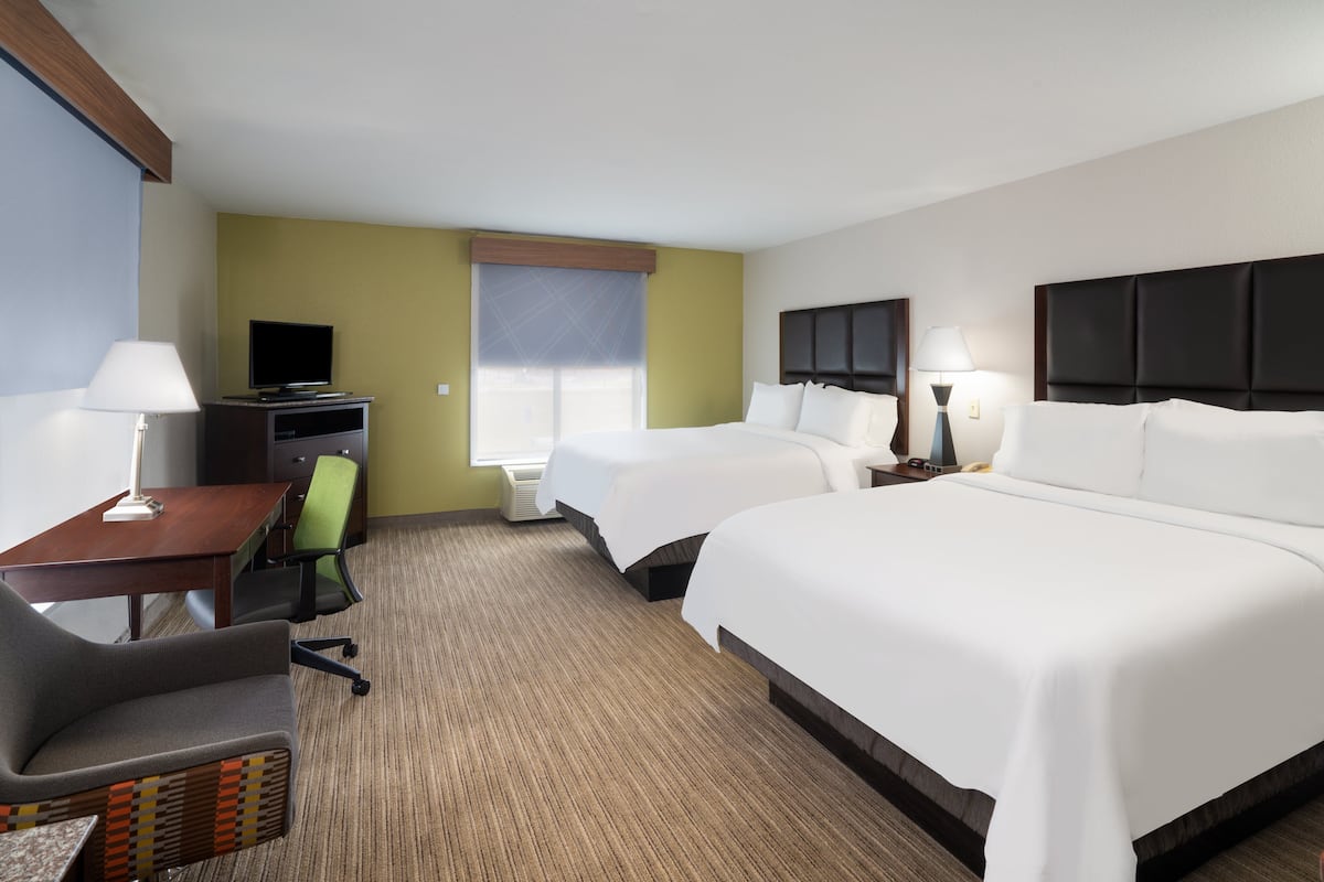 A hotel room with two beds, a desk with a chair, a television, and a window with blinds.
