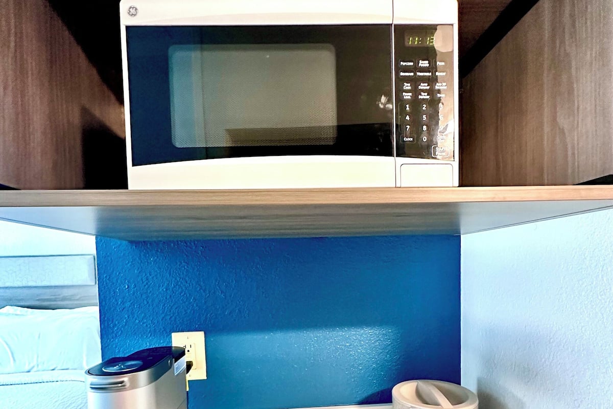 A kitchenette with a microwave, coffee maker, and yogurt containers.
