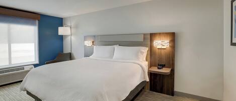 Una habitación de hotel moderna con una cama grande, una mesita de noche con lámpara y una ventana con persianas.