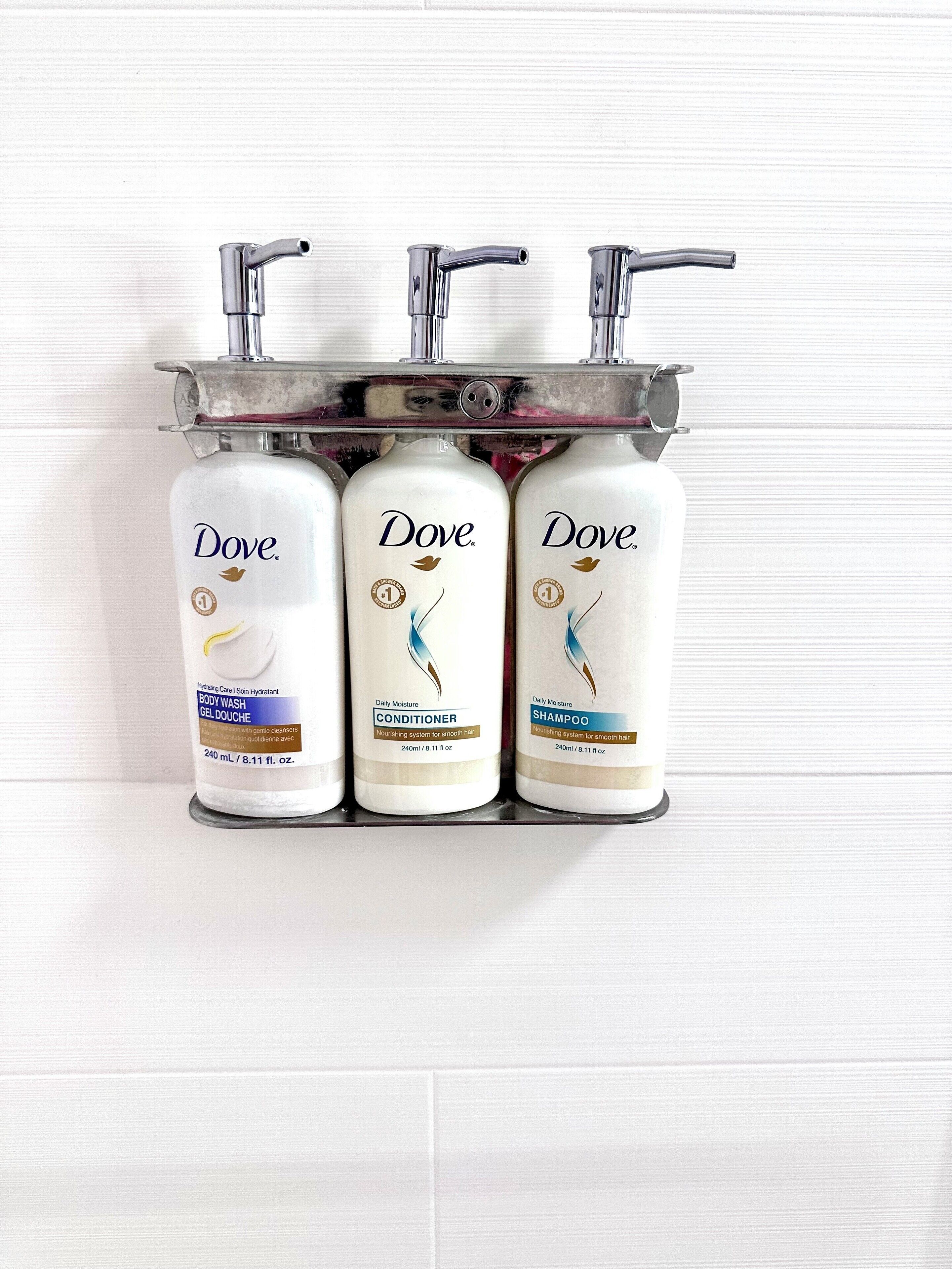 Three Dove personal care products in a metal dispenser against a white tiled wall.