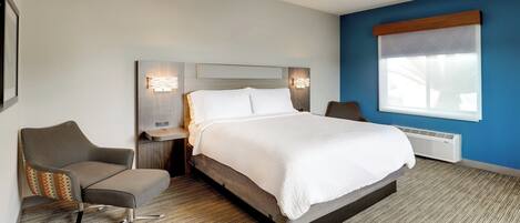 A hotel room with a large bed, a chair, a nightstand, and a window with blinds.