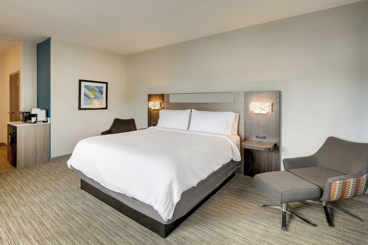 A modern hotel room with a large bed, a desk with a chair, and a sofa.