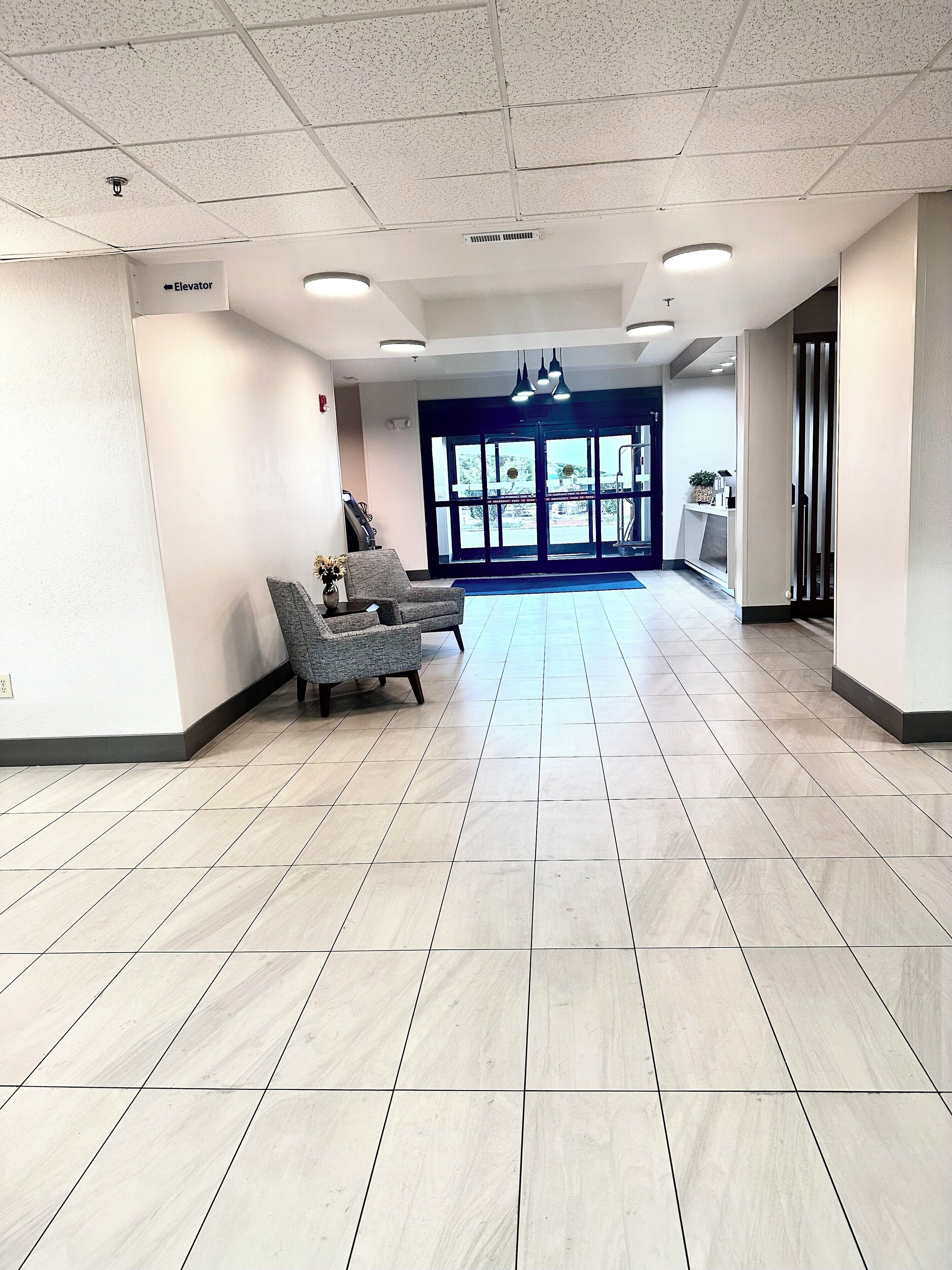 A spacious lobby with a reception desk, a waiting area with chairs, and a clear view of the outside through large doors.