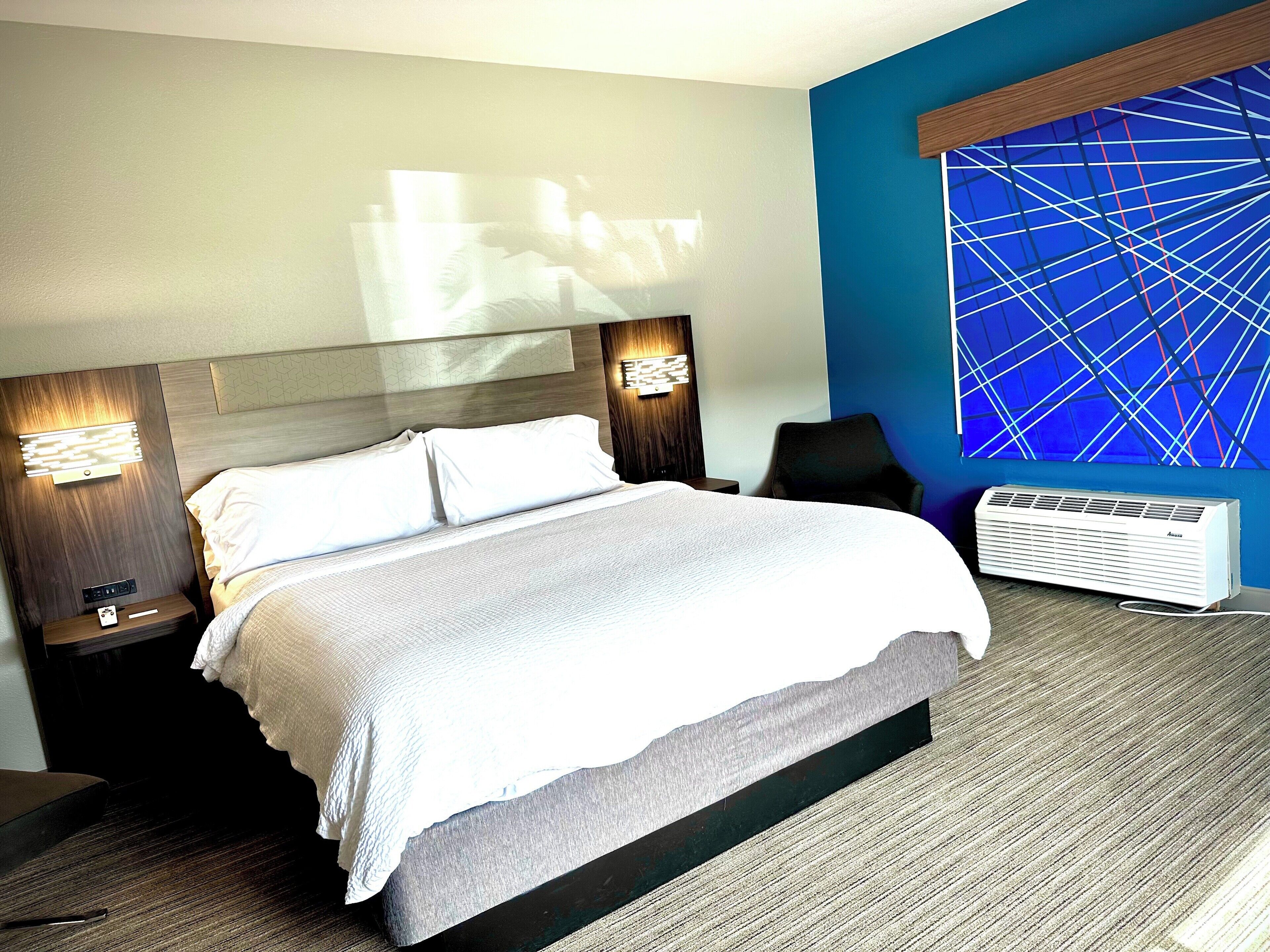 Une chambre d’hôtel avec un grand lit, deux tables de chevet avec des lampes, un climatiseur fixé au mur et un mur orné d’un motif géométrique.