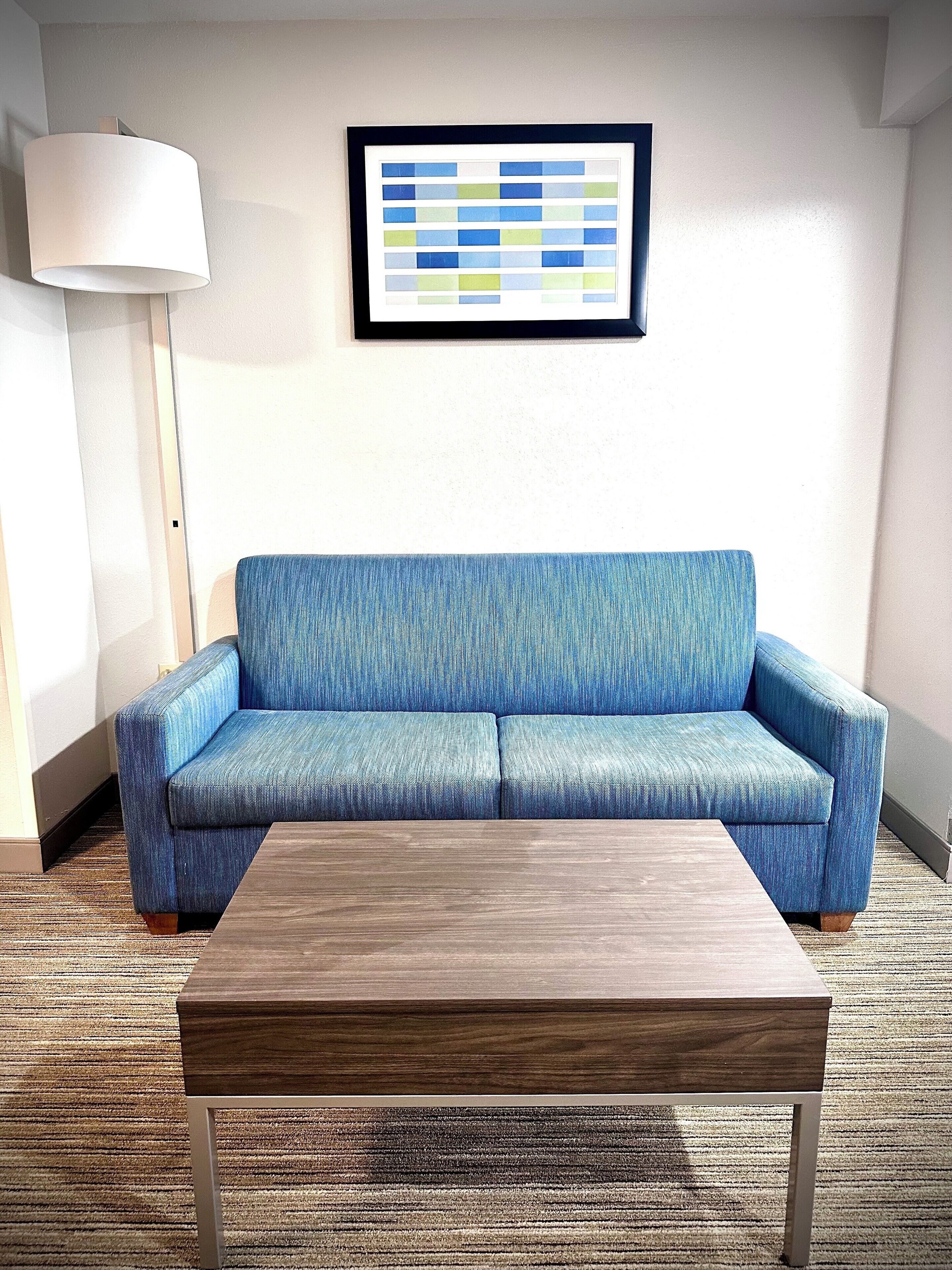 A room with a blue sofa, a wooden coffee table, a framed abstract art piece, and a floor lamp.