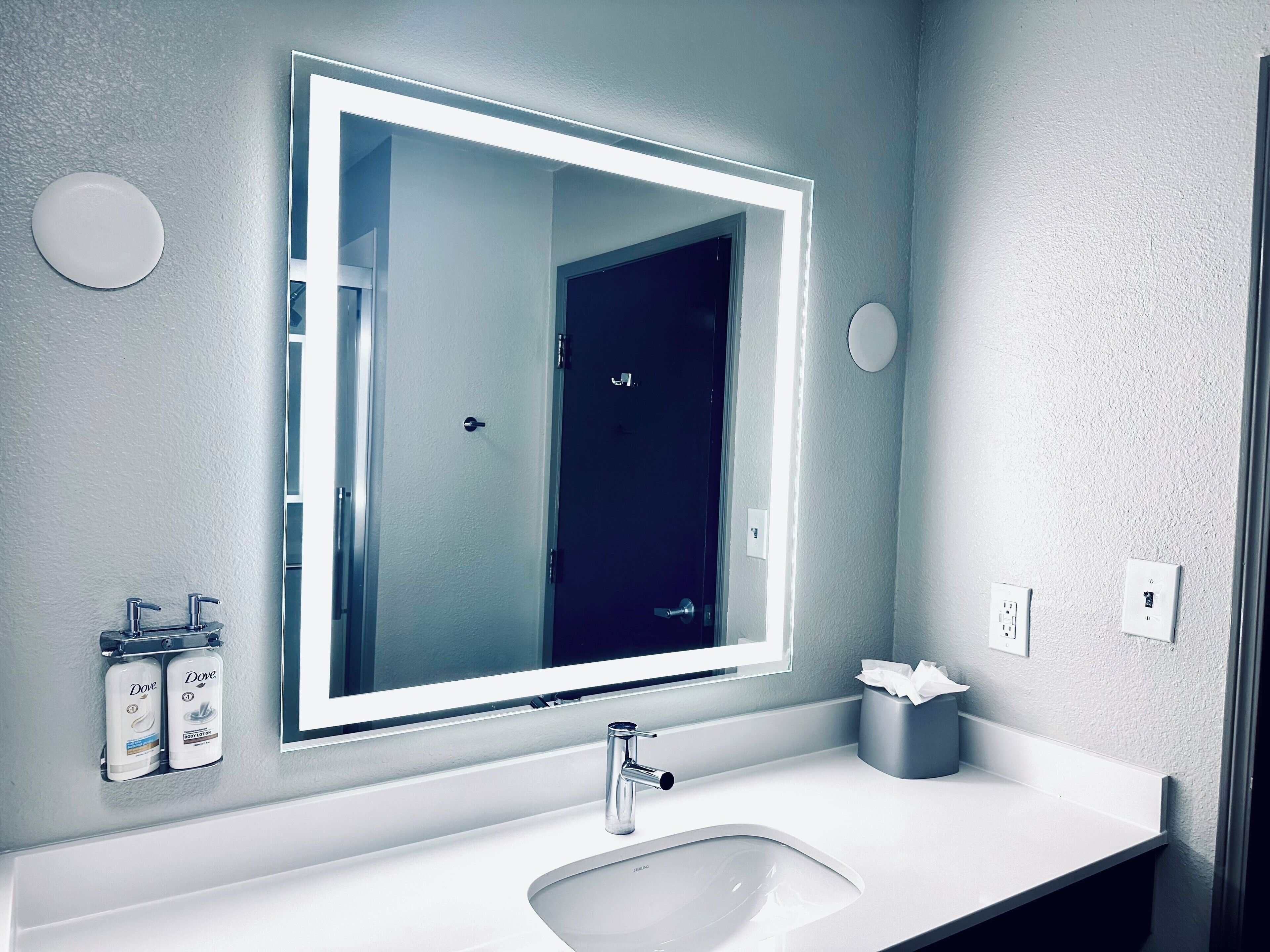Bany amb un mirall gran, un lavabo i dispensadors de loció corporal Dove.