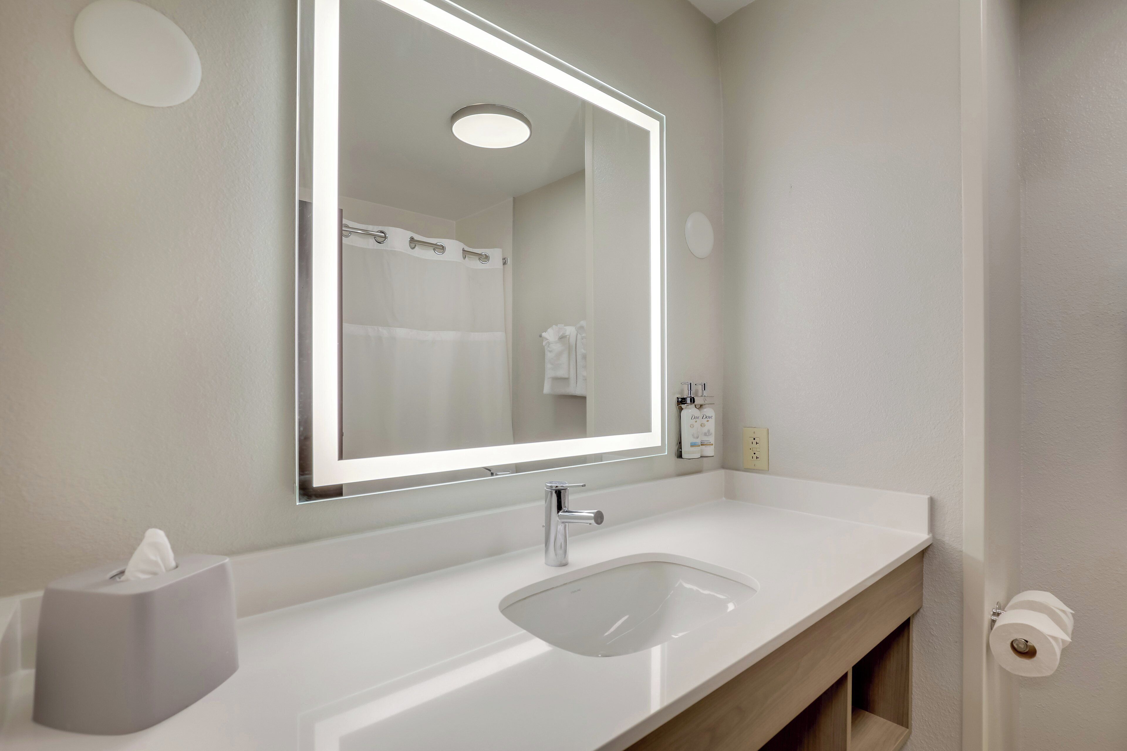 Een moderne badkamer met een grote spiegel, een witte wastafel en een handdoekdispenser.
