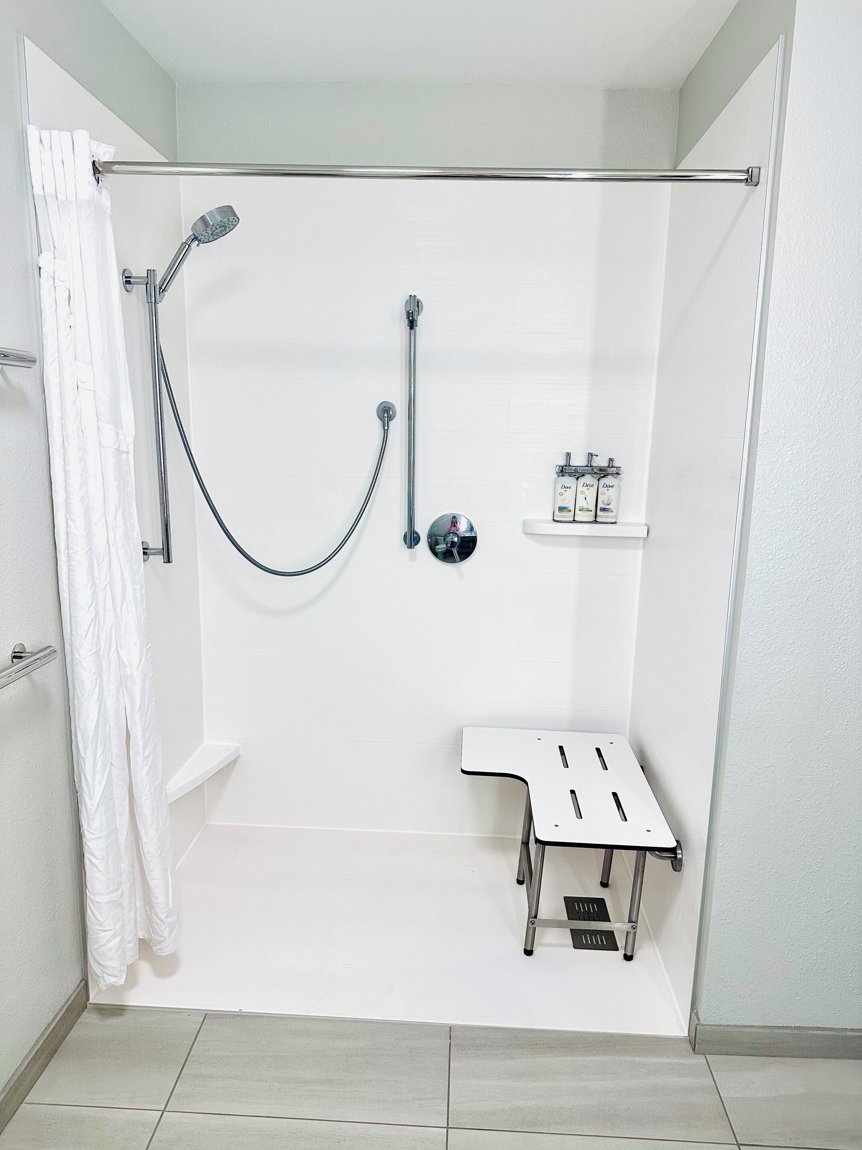 Un espacio de ducha moderno con cabezal de ducha de mano, grifo empotrado en la pared y un accesorio de ducha manual. Hay un estante pequeño con artículos de aseo y un banco blanco con desagüe.