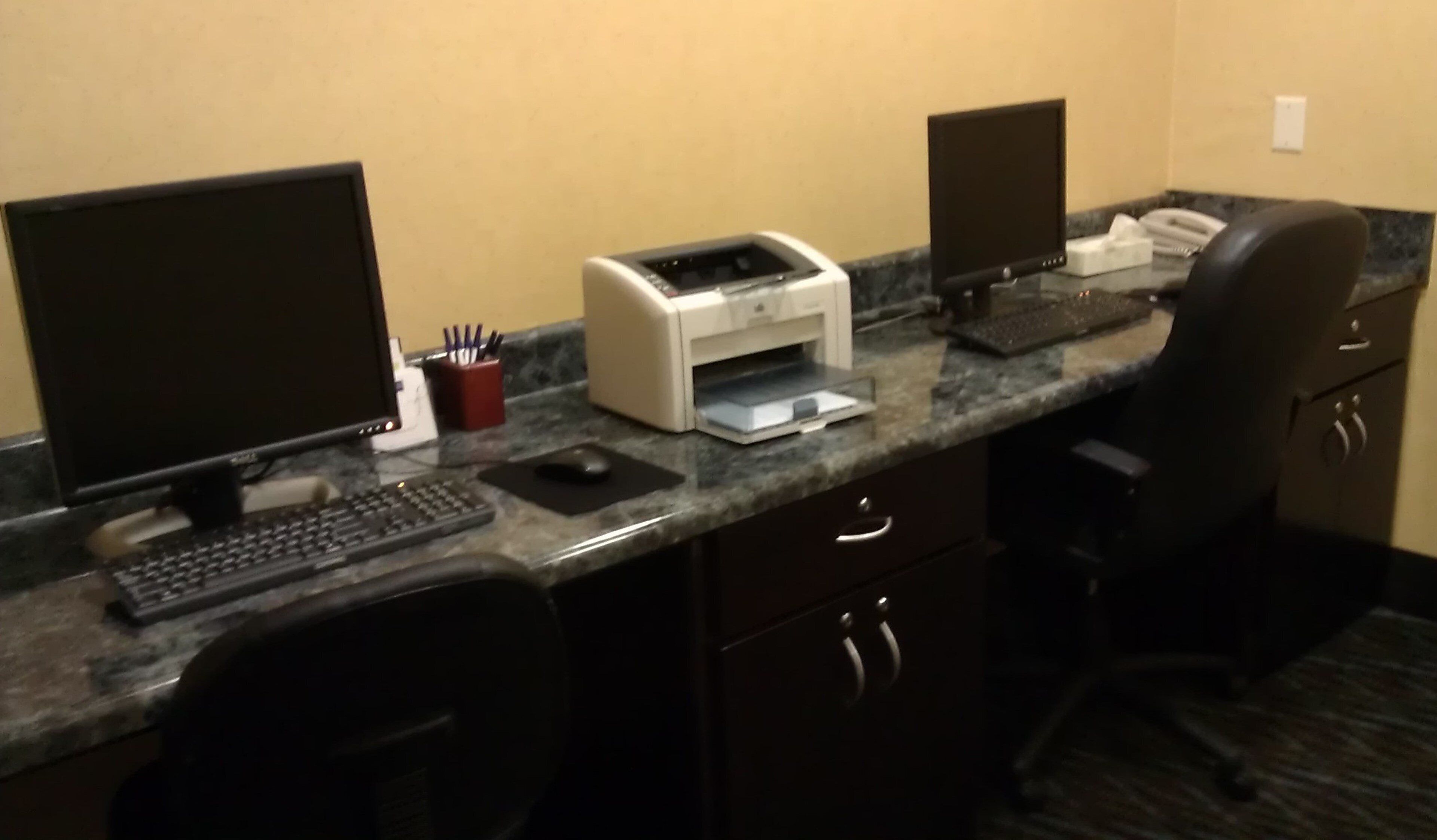 A hotel office area with a desktop computer, a printer, a telephone, and a chair.