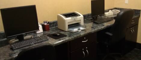 Un área de recepción de hotel con un ordenador de escritorio, una impresora, un teléfono y una silla.