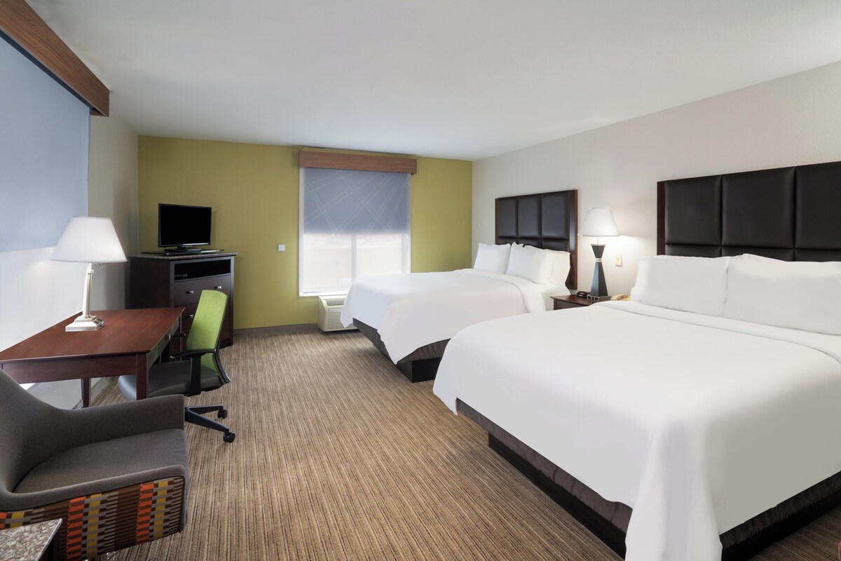 A hotel room with two beds, a desk with a chair, a television, and a window with blinds.