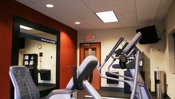 A gym with exercise equipment, a clock, and an exit sign.