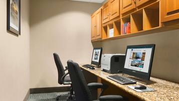 A hotel office with two computer workstations, chairs, and wooden cabinets.