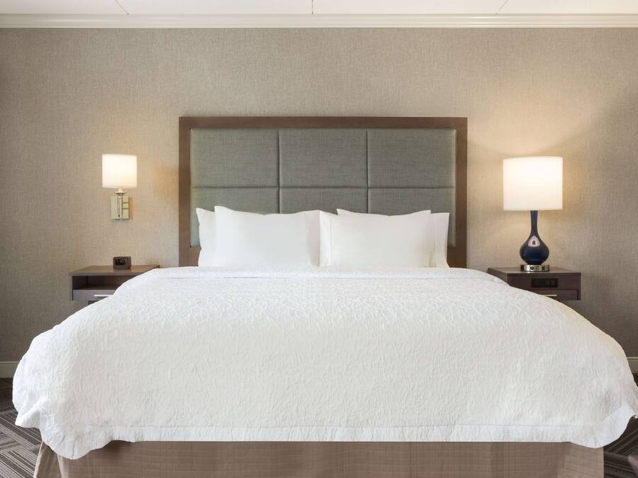 Una habitación de hotel con una cama grande, dos mesitas de noche y dos lámparas fijadas a la pared.