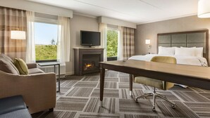 A hotel room with a bed, a desk, a TV, a fireplace, and a view of the outdoors. - Hampton Inn & Suites Manchester-Bedford (Bedford)