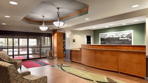 A hotel reception area with a wooden reception desk, a large window, and a reception desk with a 'thanks' sign. - Hampton Inn & Suites Manchester-Bedford (Bedford)