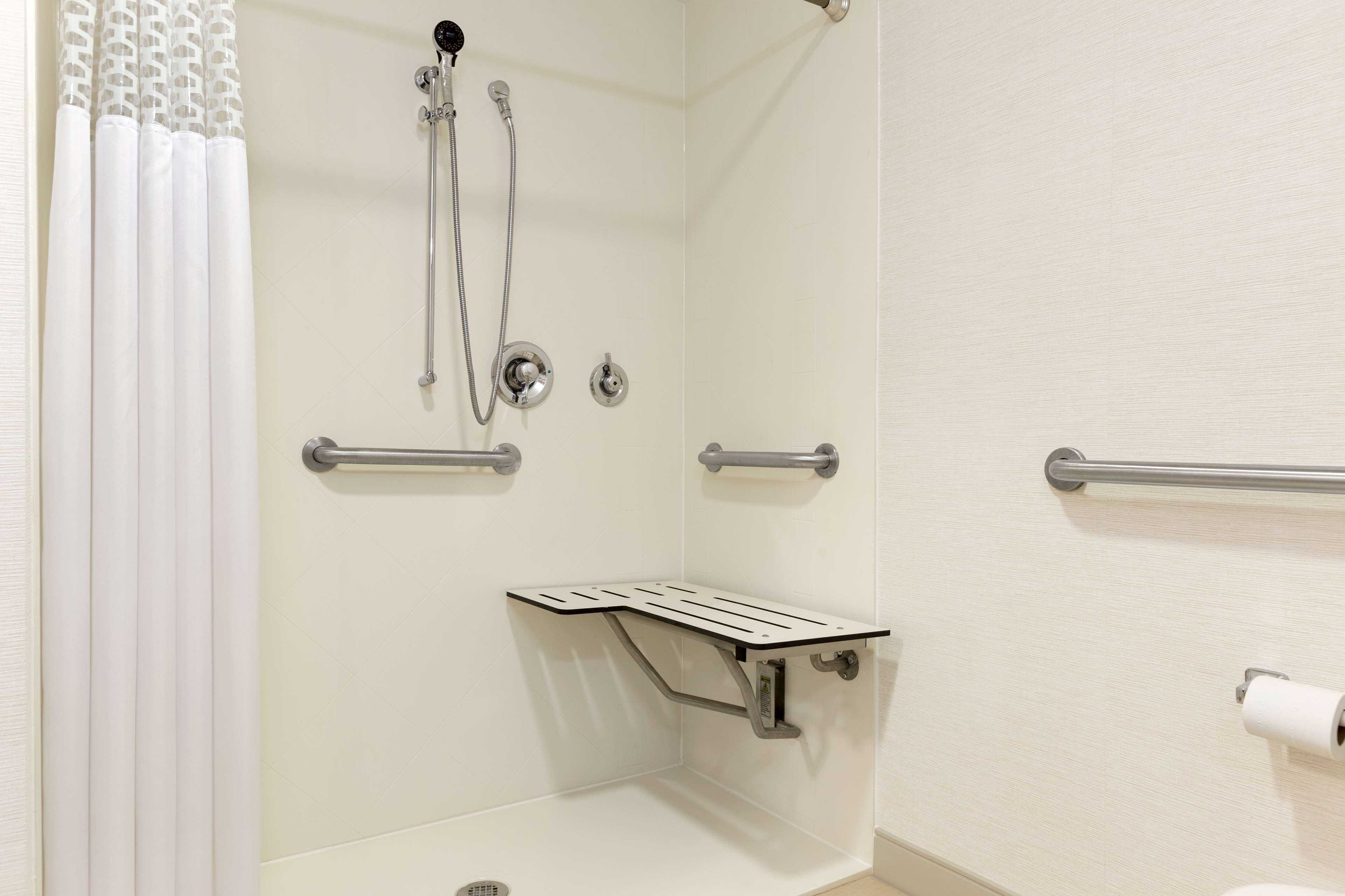 A bathroom with a shower, grab bars, a toilet, and a towel rack.