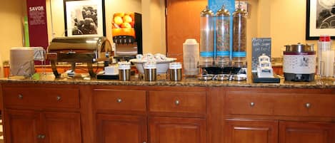 A hotel reception area with a coffee station, snack bar, and a large framed picture on the wall.