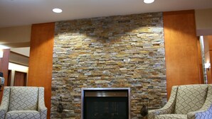 A room with a stone wall, two patterned armchairs, and a fireplace. - Hampton Inn & Suites Manchester-Bedford (Bedford)
