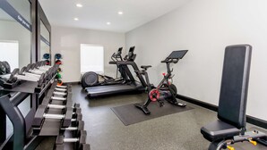 Een sportschool met trainingsapparatuur, waaronder loopbanden, een elliptische trainer en losse gewichten.