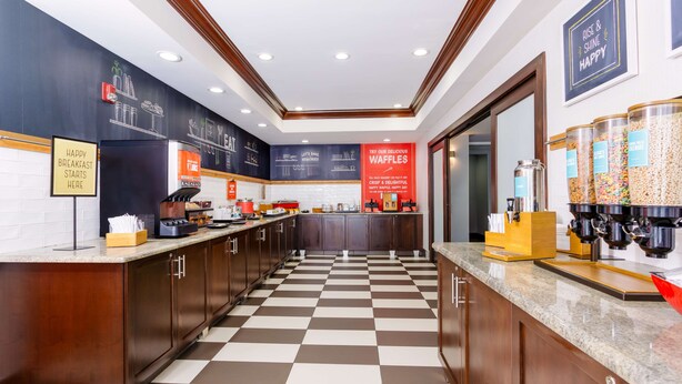 Een moderne keuken met een geruit vloertje, houten keukenkastjes en een pannenkoekenstation.