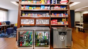 Een drankje en hapjesstand in een hotellobby met gevulde planken voor snacks en drankjes, en twee gekoelde vitrines.